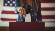 voter submitting a ballot flanked by U.S. flag